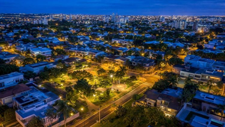 Vista aérea de loteamento urbano regular plenamente implantado ao entardecer, com ruas pavimentadas, iluminação, praça e lotes edificados conforme a Lei 6.766/79
